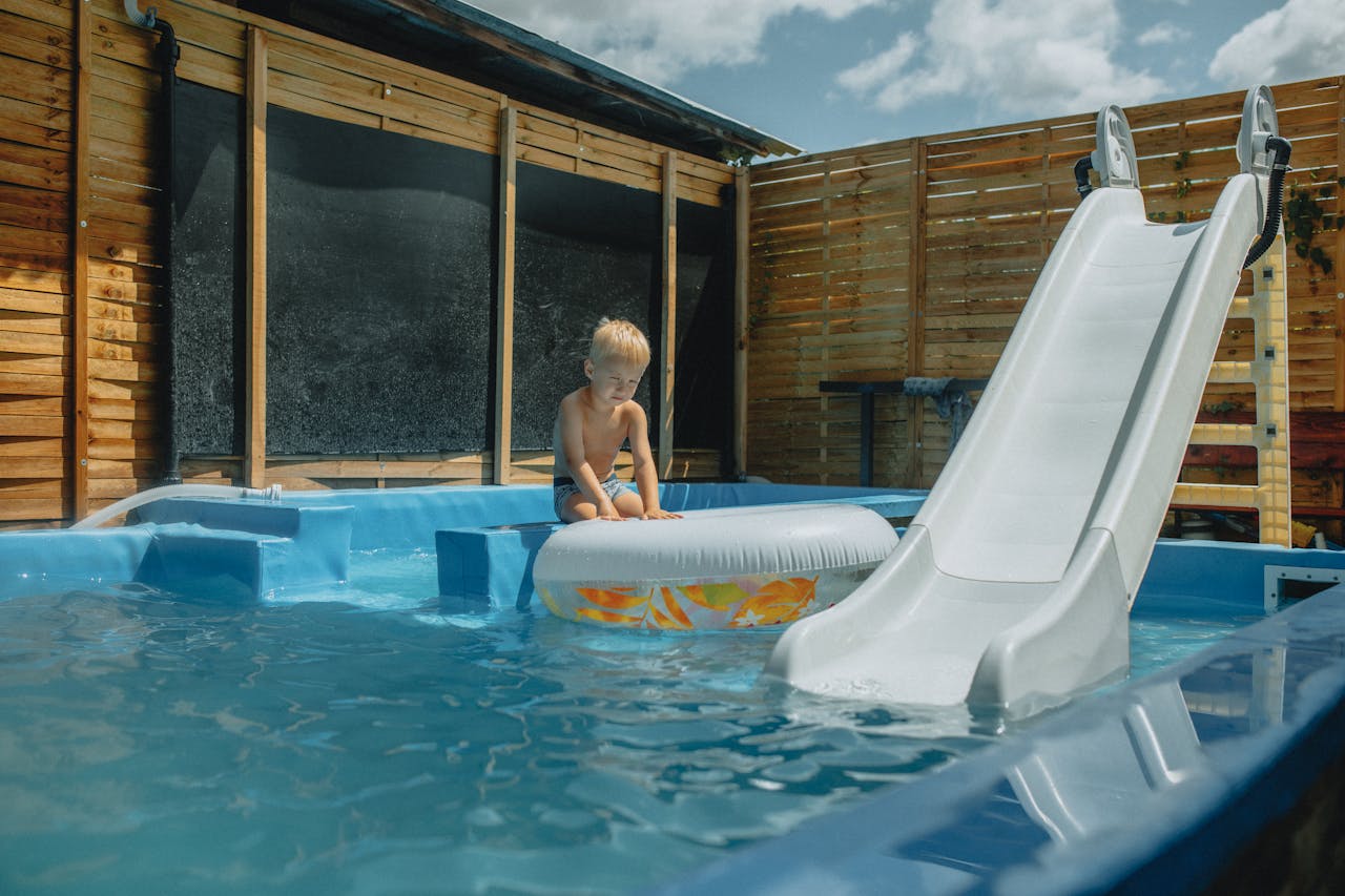 Young child playing with inflatable in a pool with slide during summer.